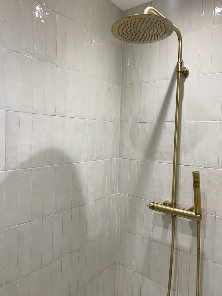 Douche moderne avec carrelage blanc et robinetterie dorée haut de gamme